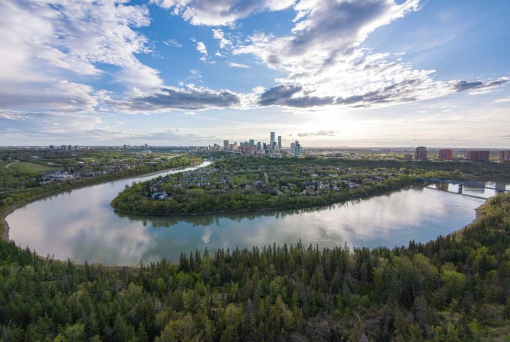 East, looking west: the North Saskatchewan River snakes a "U" around Edmonton's skyline on a sunny day broken by a few clouds.